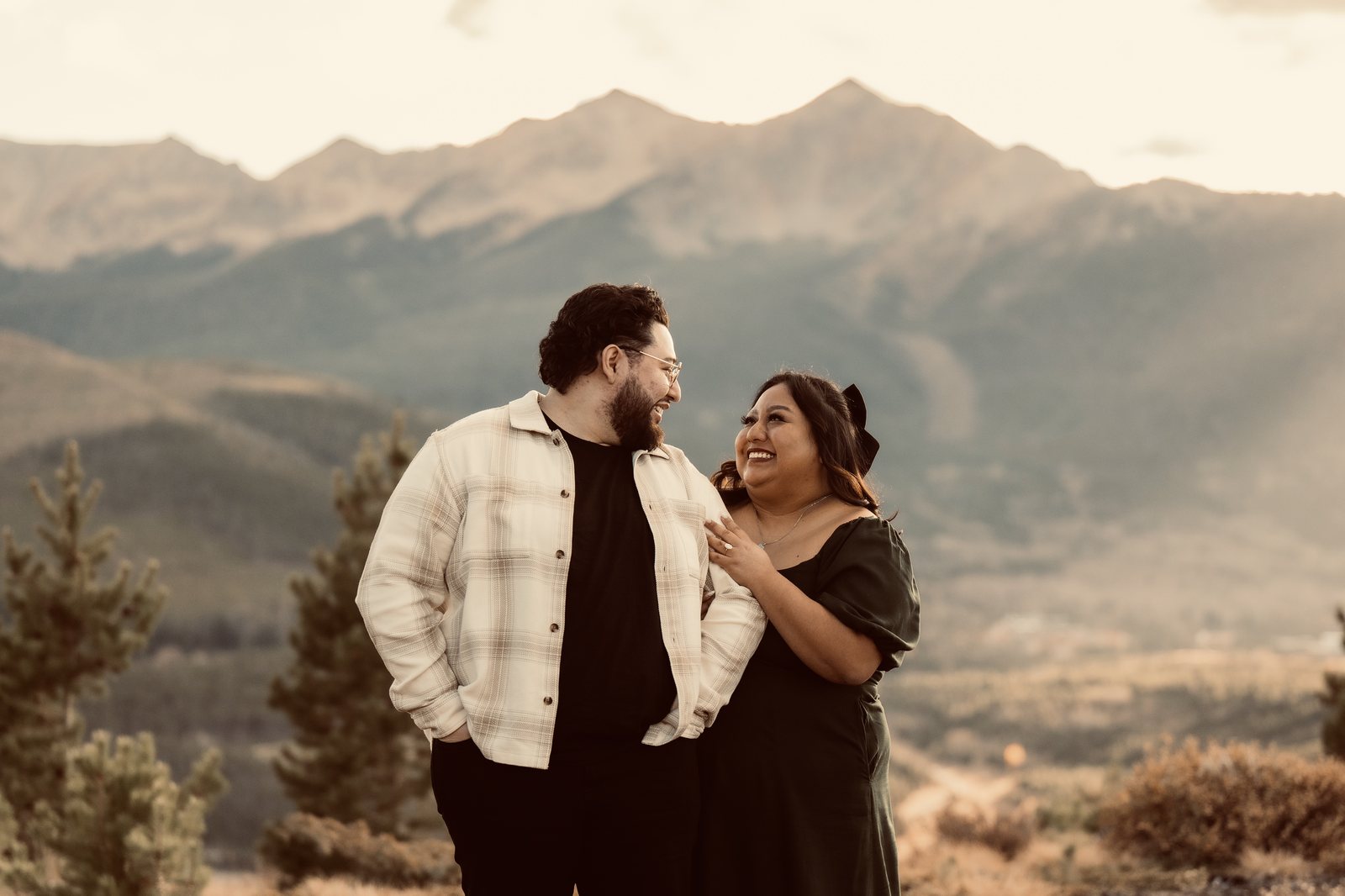 Juan and his fiancée Kymm laughing together on a mountainside at sunset, Colorado in the background.