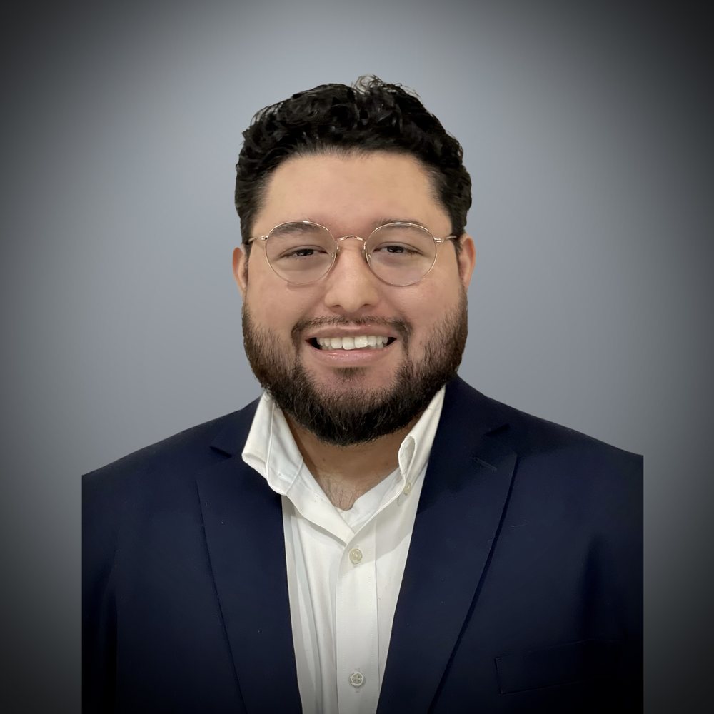 Juan Tellez smiling in a navy jacket and glasses.